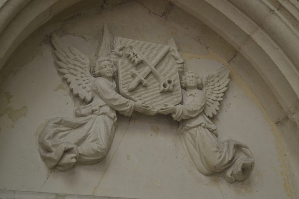 Photo de deux anges en pierre blanche sculptée qui portent un blason