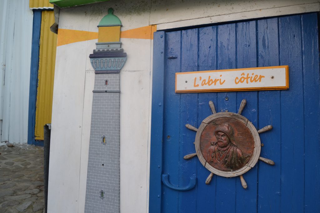 Photo d'une des cabane très décorée avec inscrit "L'abri côtier" avec un petit phare en décoration