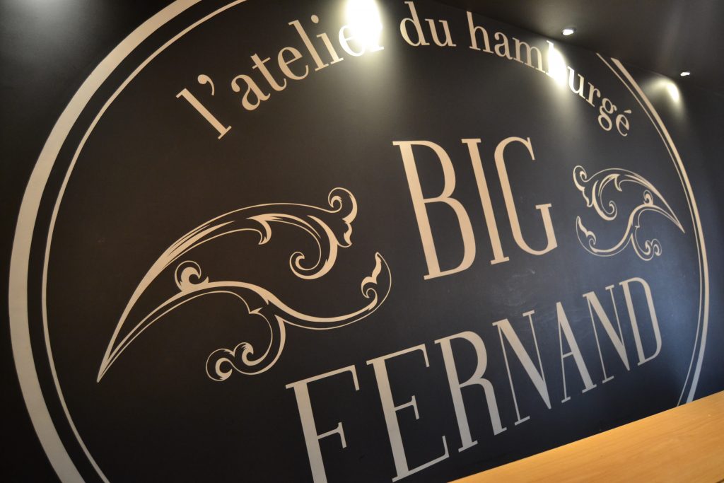 Photo d'un mur noir où est inscrit "l'atelier du hamburgé" et "Big Fernand"